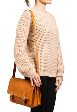 Borsa a tracolla in pelle marrone con due fibbie, tracolla regolabile, forma rettangolare e superficie liscia, tenuta da una persona in un maglione beige.