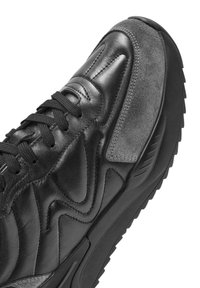 Sneaker nera caratterizzata da una combinazione di pelle liscia e suede, design sagomato, cuciture testurizzate e suola in gomma con dettagli accentuati.