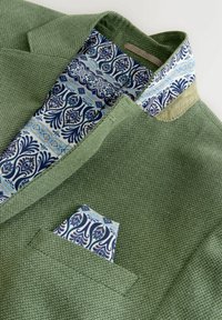 Groene gebreide blazer met blauwe en witte patroonvoering en bijpassend pochet, getoond op een witte achtergrond.