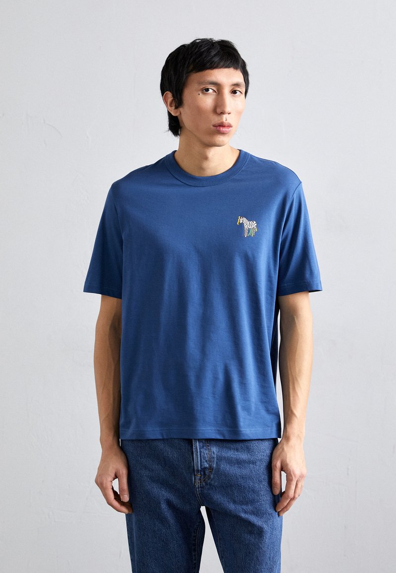 Mėlynas medvilninis marškinėliai su apvaliu iškirpimu ir trumpomis rankovėmis, su mažo siuvinėjamo zebrų dizainu kairėje krūtinės pusėje.