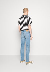 Raitapaitainen mustavalkoinen lyhyt t-paita, vaaleansiniset farkut ja beige kenkäpari. Farkuissa on nahkahuopa takakujalla.