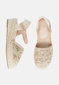 Sandali espadrilles beige con texture intrecciata, cinturini in pelle e suola platform. I dettagli includono cuciture decorative e una fibbia alla caviglia.