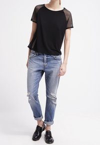 Musta verkkohihainen T-paita rentoa leikkausta, yhdistettynä vaaleansiniisiin kulutettuihin farkkuihin ja mustiin nauhakenkiin.