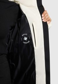 Zwart-witte pufferjack-interieur met een logo, ribbelstof in het zwart eronder, en een zijzak met een zichtbare rits.