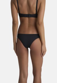 Set di bikini nero con un design semplice, caratterizzato da spalline sottili, una chiusura posteriore sicura e un fondo a copertura minima. Texture liscia e opaca.