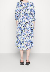 Florale midi-jurk in blauw, lavendel en groen, met driekwartmouwen, een cinched taille en een vloeiende zoom. Vierkante haksandalen.