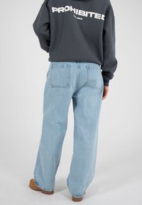 Hele sinise värvusega laia lõikega teksapüksid, mis on valmistatud teksariidest, kahe tagataskuga ja lõdva istuvusega, kombineeritud tumedat halli dressipluusiga.