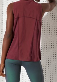 Bordowy top bez rękawów z teksturowanym wykończeniem, z wysokim dekoltem i luźnym krojem, zestawiony z zielonymi legginsami.
