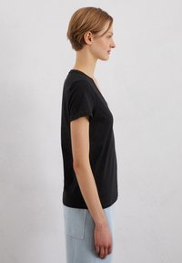 Czarna koszulka krótki rękaw, dekolt w serek, slim fit, miękka faktura, noszona z jasnoniebieskimi spodniami o wysokim stanie, widok z boku na neutralnym tle.