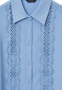 Chemise bleu clair à boutons avec un col, présentant des détails en dentelle élaborés sur le devant et une texture de tissu lisse. Taille S.