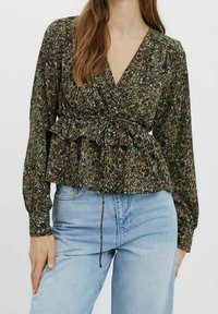 Zelená halenka s květinovým potiskem, dlouhými rukávy, zavinovacím střihem a řaseným lemem. Kombinováno s světle modrými džíny s vysokým pasem.