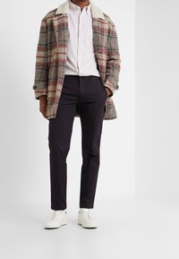 Wełniany płaszcz w kratę z białym kołnierzem z baraniny, wzór w odcieniach szarości i czerwieni; jasnoróżowa koszula na guziki; ciemne spodnie; białe tenisówki.