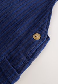 Navy blue fabric with vertical stripes, featuring a textured weave. Includes a round, tan button with a cross design, stitched on the side.