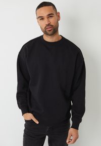 Zwarte sweatshirt met een ronde hals, lange mouwen en ribgebreide boorden. De stof lijkt zacht en gestructureerd. Draag het over een donkere spijkerbroek.