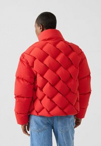 Rote Stepp-Steppjacke mit einem hohen Kragen, die eine glatte Textur zeigt. Kombiniert mit hellblauen Jeans.