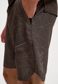 Bruna idrottsshorts med ett geometriskt mönster i ljusrosa, med en logotyp och sned fåll. Tillverkade av lätt, mjukt material.