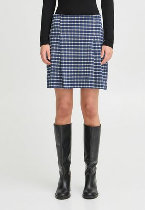 Jupe à carreaux bleus et blancs avec des plis, en tissu, associée à des bottes en cuir noires jusqu'aux genoux.