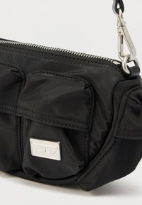 Sort nylonveske med glidelåslukking, utstyrt med to frontlommer og en sølvfarget logodetalj. Teksturert overflate og sølvdetaljer i metall.