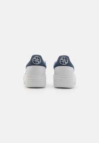 Blaue und weiße Sneakers mit einem glatten Lederobermaterial, gepolstertem Kragen und dicker weißer Sohle. Verfügt über ein Logo auf der Fersenkappe.