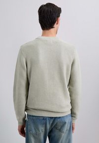 Pull en maille vert clair avec un tissu texturé, col rond et poignets et ourlet côtelés, porté avec un jean en denim bleu.