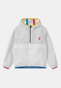 Vit vindjacka med ett geometriskt grått mönster, gul huva inuti och färgglada detaljer i blått, rött och svart. Har en framficka och dragkedja.