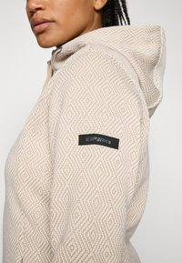 Felpa beige con motivo a diamante testurizzato, dotata di un patch logo nero sul maniche e un cappuccio rimovibile.