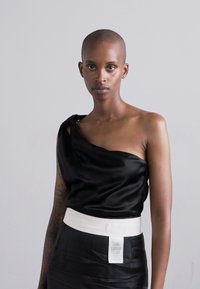 Melnas satīna blūze ar asimetrisku dizainu, kurai ir viens pliks plecs un balts josta. Iekļauts redzams kopšanas marķējums.