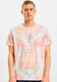 Short-sleeve T-shirt in light colors with a pastel geometric and palm tree pattern; features a circular logo design at the center.