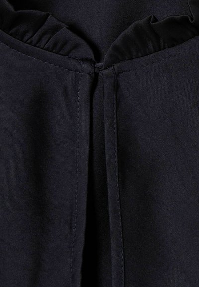 Primer plano de una tela negra con una costura vertical central y un detalle de volante fruncido en el borde superior.