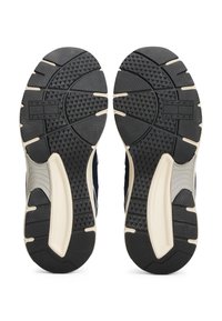 Podeszwy czarnych i beżowych sneakersów z teksturowanym gripem oraz widoczną marką "Tommy Jeans" na każdej podeszwie, pokazane obok siebie.
