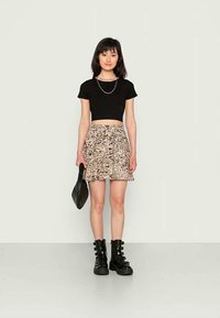 T-shirt cropped preto, saia mini bege com padrões, botas de combate pretas com fivelas e uma bolsa de ombro preta. Design simples e moderno.