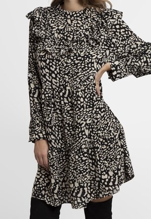 Robe à motifs noir et beige avec un col volanté et des manches longues, présentant une jupe à volants et une texture de tissu léger.