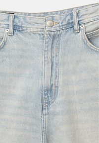 Nahaufnahme der Taille einer hellblauen Denim-Jeans mit Metallknopf, Gürtelschlaufen, Vordertaschen und sichtbaren Nähdetails.