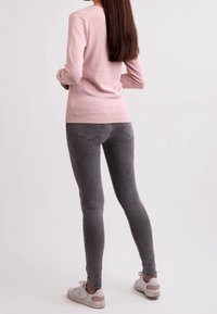 Ljusrosa långärmad topp i kombination med grå slim-fit jeans och vita sneakers med rosa detaljer. Särskilt mjuk textur, enkel design.