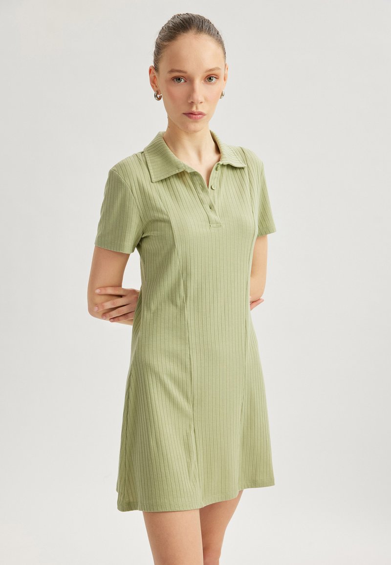 Vestido de manga corta con cuello en tejido acanalado de color verde claro. Presenta una fila de botones y cae por encima de la rodilla, con un diseño ajustado.