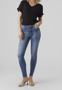 Schwarzes, kurzärmliges V-Ausschnitt-Oberteil, kombiniert mit hellblauen, schmalen Jeans mit mittelhohem Bund und dezentem Verblassen, ergänzt durch nudefarbene High Heels.