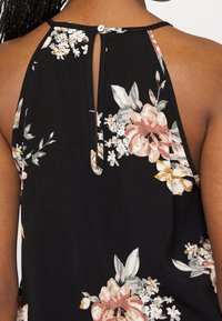 Haut en tissu noir avec un motif floral rose, blanc et jaune, doté d'une ouverture en forme de goutte dans le dos et d'une fermeture par bouton au niveau du col.