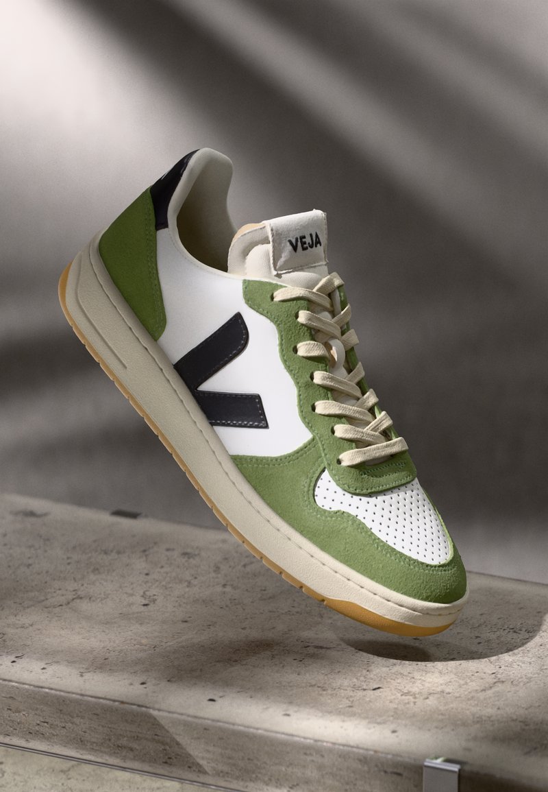 Hvit sneaker med grønne og marineblå detaljer, med en teksturert overflate, perforert tå og beige såle. "VEJA"-logo på tungen.