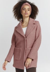 Rosa ullkappa med indragen krage, framknäppning med knappar och två stora fickor fram. Slät textur och avslappnad passform.