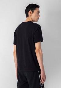 Camiseta de algodón negra con cuello circular, mangas cortas y un diseño simple. La tela tiene una textura suave y un ajuste casual.