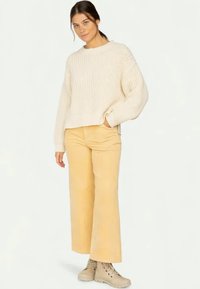Beige neulepaita, jossa on rento malli, yhdistettynä vaaleankeltaisiin leveälahkeisiin housuihin ja beigeihin nilkkureihin. Rakenne on löysä ja mukava.