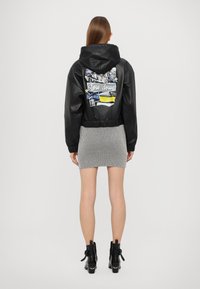 Schwarze Leder-Bikerjacke mit Kapuze, die mit einem bunten Grafikdesign auf dem Rücken versehen ist, getragen über einem gestreiften Minirock und schwarzen Ankle Boots.