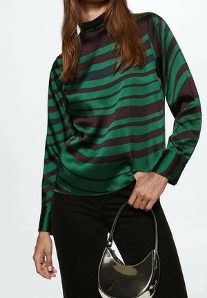 Bluzka z długim rękawem w zielono-czarne paski, wykonana z gładkiej tkaniny, z wysokim dekoltem, zestawiona z czarnymi spodniami i małą błyszczącą torebką.