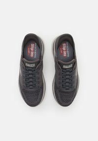 Zapatillas de deporte Skechers grises sin cordones, con una parte superior de punto texturizado, cordones y plantilla acolchada, que presentan un logo sutil en el costado y el talón.