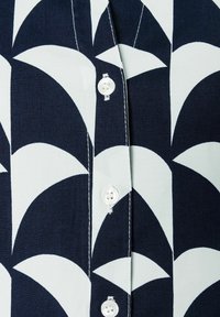 Dunkelblaues und hellblaues Hemd mit einem geometrischen Muster aus geschwungenen Formen, ausgestattet mit einer Knopfleiste, die weiße Kunststoffknöpfe präsentiert.