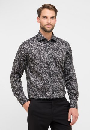 Schwarzes Langarmhemd mit weißem und rosa floralem Paisleymuster, mit Kragen und strukturiertem Stoff, kombiniert mit schwarzen Hosen.
