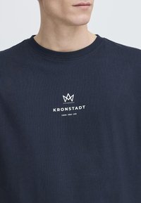 Marineblå bomullssweatshirt med rund hals, med en hvit logo som leser "KRONSTADT" og et kronegrafikk over.