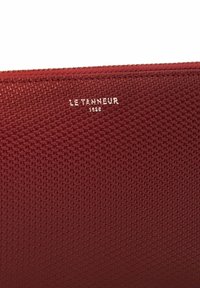 Portafoglio rosso con una texture e un sottile motivo geometrico, caratterizzato da un logo impresso in argento "LE TANNEUR 1898" sul davanti.
