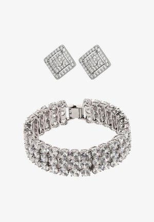 Pendientes cuadrados adornados con diamantes, combinados con una pulsera ancha de plata que presenta dos filas de grandes piedras preciosas redondas y claras.