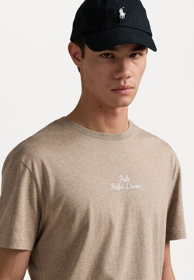 Μπεζ βαμβακερό μπλουζάκι με κοντά μανίκια, με λευκό κεντημένο λογότυπο. Μαύρο καπέλο με λογότυπο μπροστά, σχεδιασμένο με επίπεδη σκεπή.